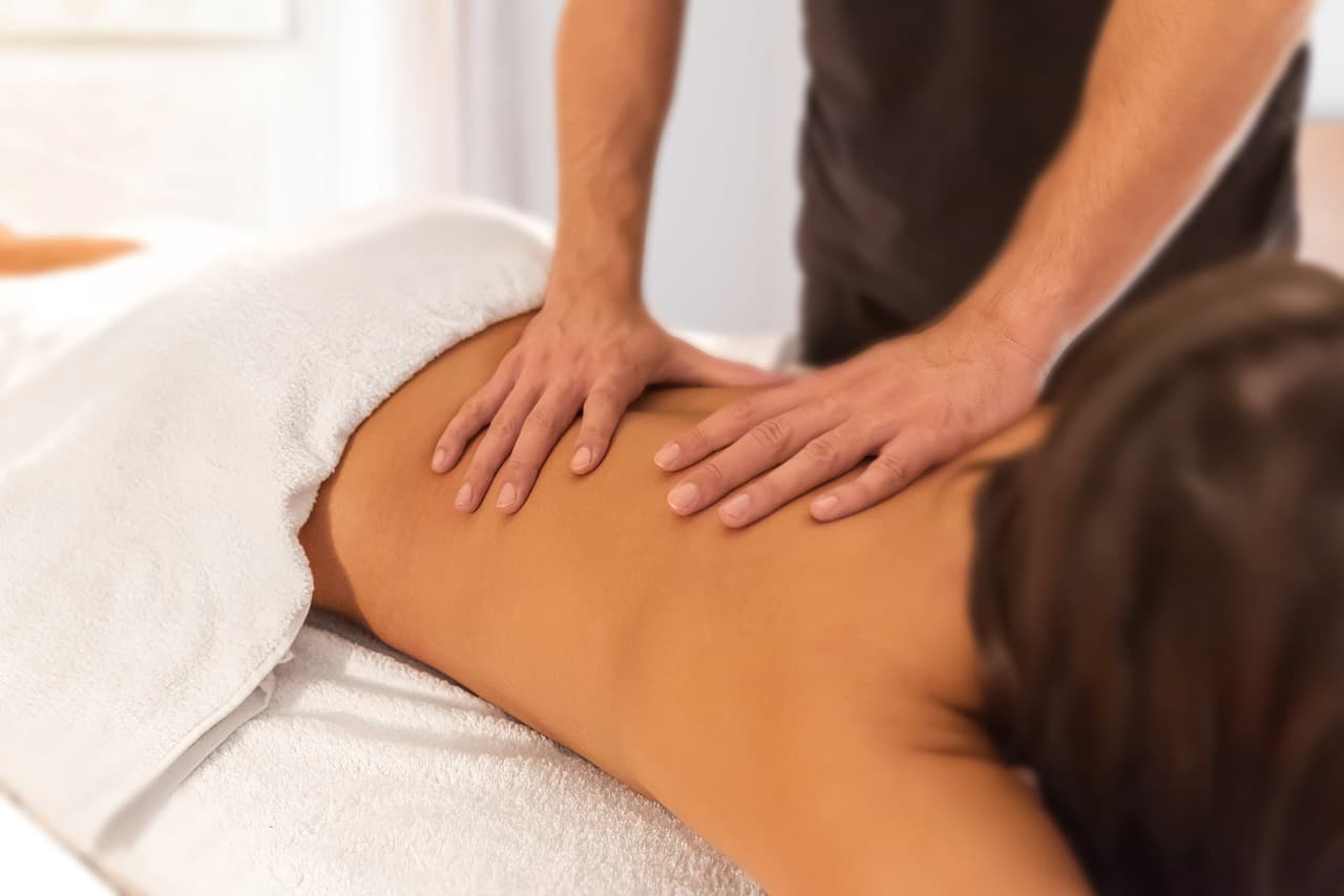 A therapist’s hands massaging a client’s back on a towel-covered bed