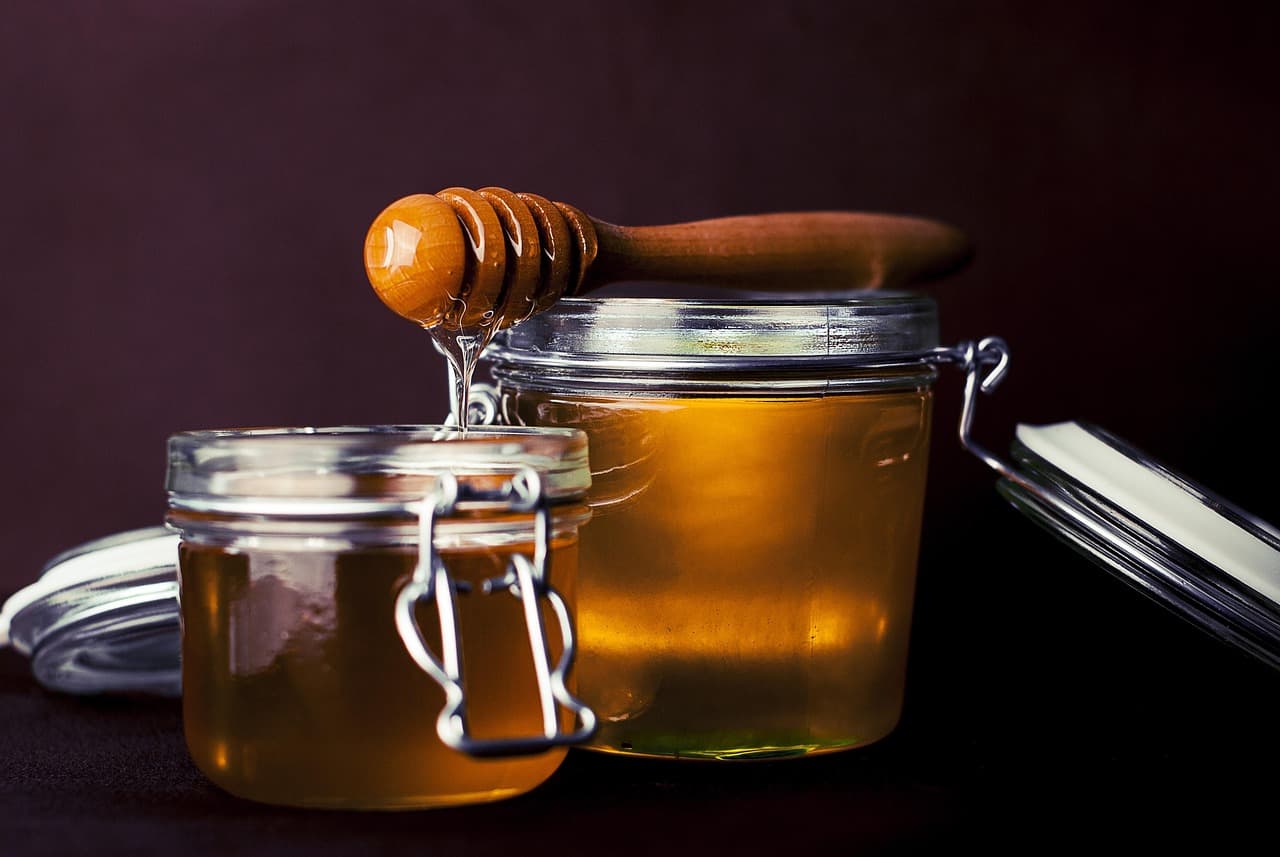 Two jars of golden honey with a wooden dipper